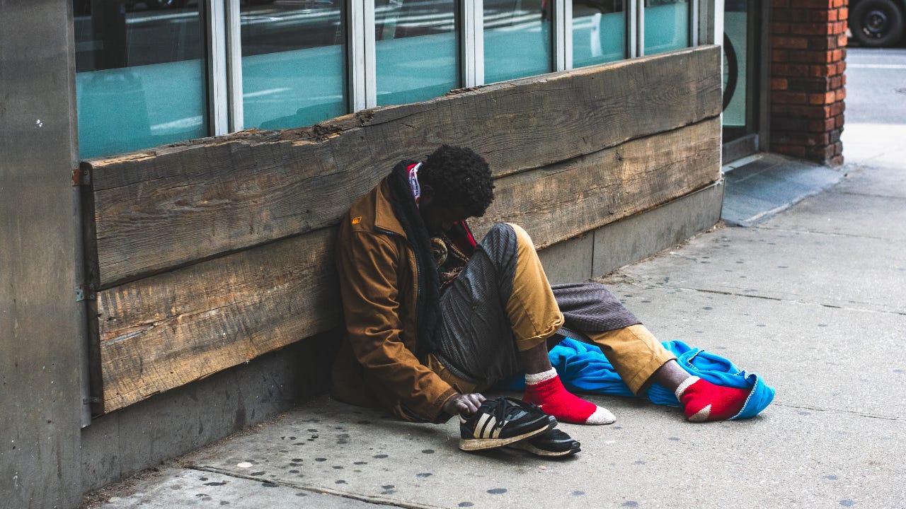 A homeless man sitting on the sidewalk. A homeless man sitting on the sidewalk.