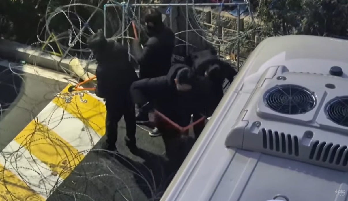 video screenshot filmed from above, showing black-clad South Korean police cutting through barbed wire outside Yoon's home in Seoul, next to them, parked perpendicular in the road, is a bus being used as part of a barricade video screenshot filmed from above, showing black-clad South Korean police cutting through barbed wire outside Yoon's home in Seoul, next to them, parked perpendicular in the road, is a bus being used as part of a barricade