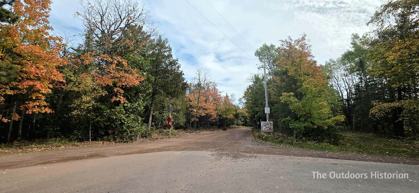 A paved cul de sac with a gravel road stretching beyond lined with trees.
