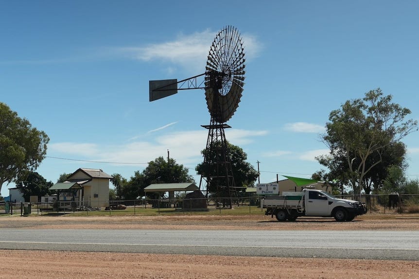 a windmill next to a road and a parked white ute a windmill next to a road and a parked white ute