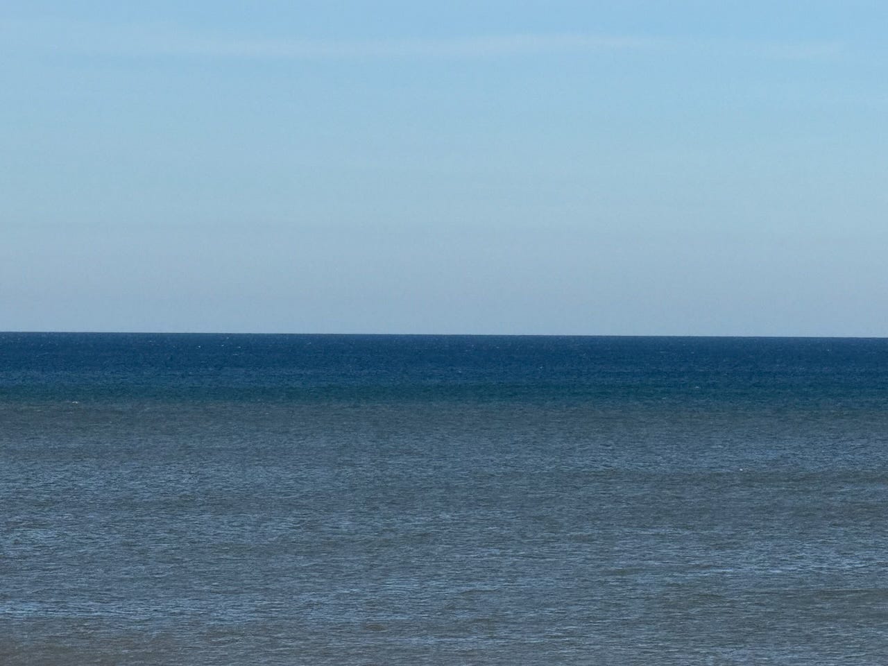 A calm view over the IJsselmeer in North Holland, with gentle ripples across the water in shades of blue and grey, meeting a clear sky at the horizon.