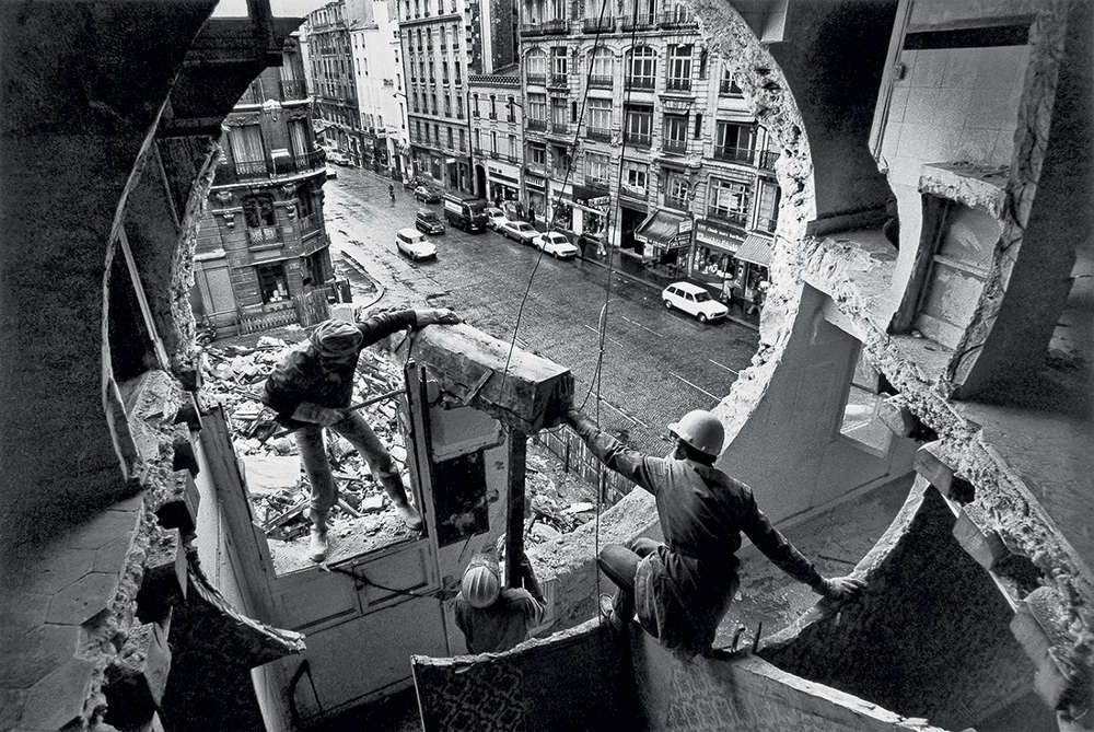 Black and white photo of a concrete building in Paris with a massive pertly circular hole cut into its side. The photographer's vantage is taken from inside the building looking out into the street which appears to be about two or three floors below. This is the handiwork of the anarchitect Gordon Matta-Clark.
