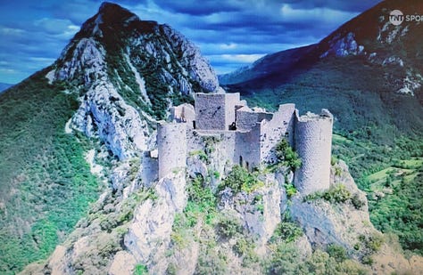 Image of a chateau on a mountain, a fan with an Alaphillippe sign, a fan wearing a t-rex costume