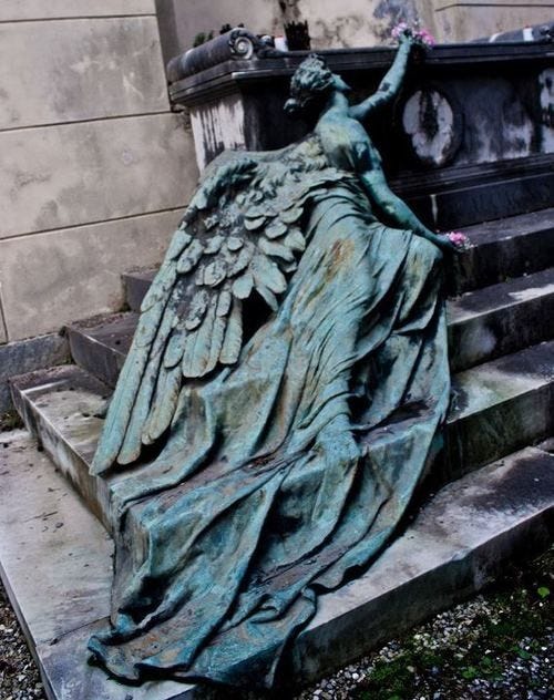 This may contain: an angel statue sitting on top of some steps next to a building with flowers growing out of it