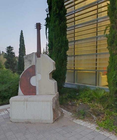 Three large stone sculptures in front of the Bet Musika: a half-guitar/half-cello; a viol, and a guitar with the faces of three musicians surrounding the instrument's neck.