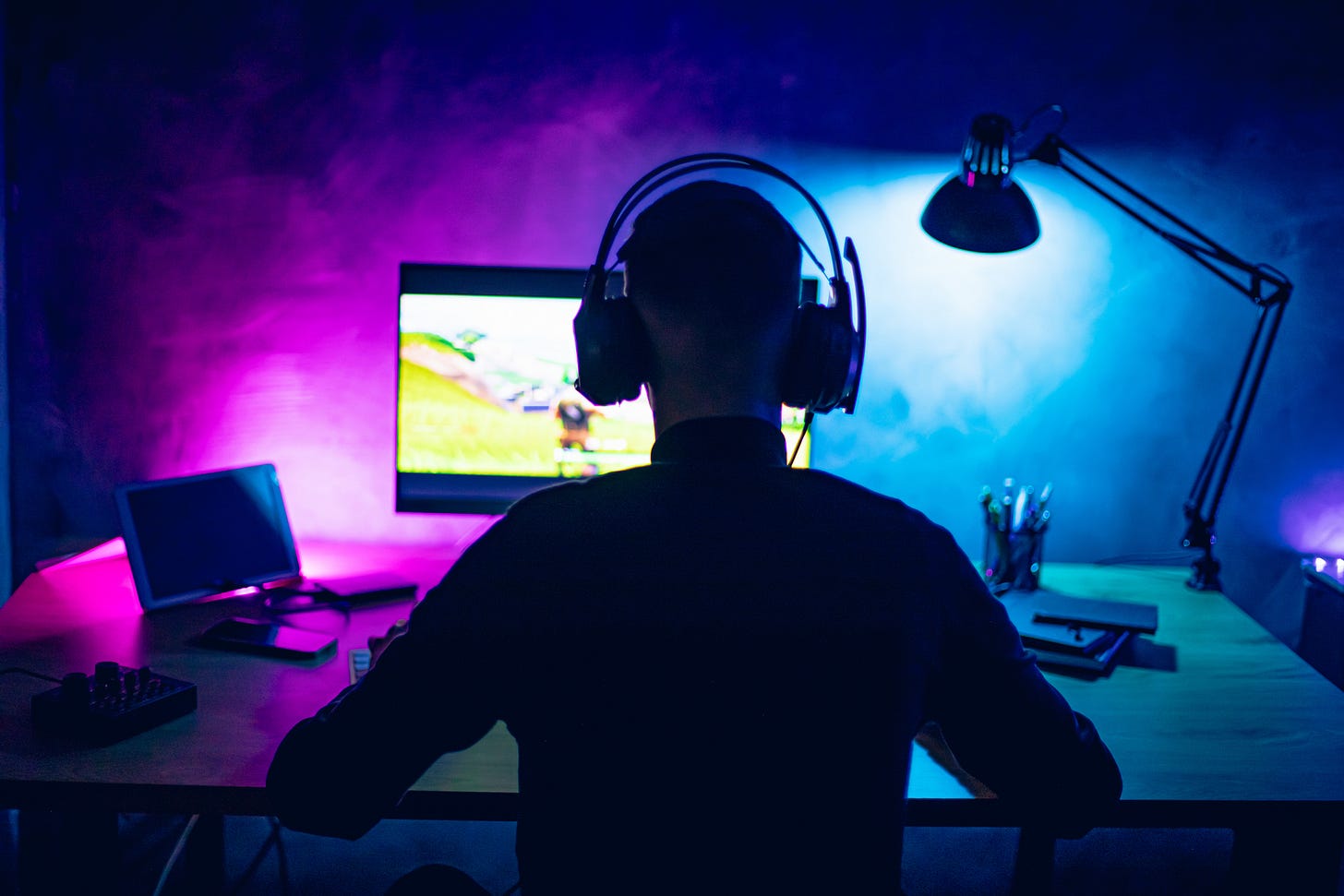 Gamer sitting in front of a bright monitor wearing headphones in a dark room