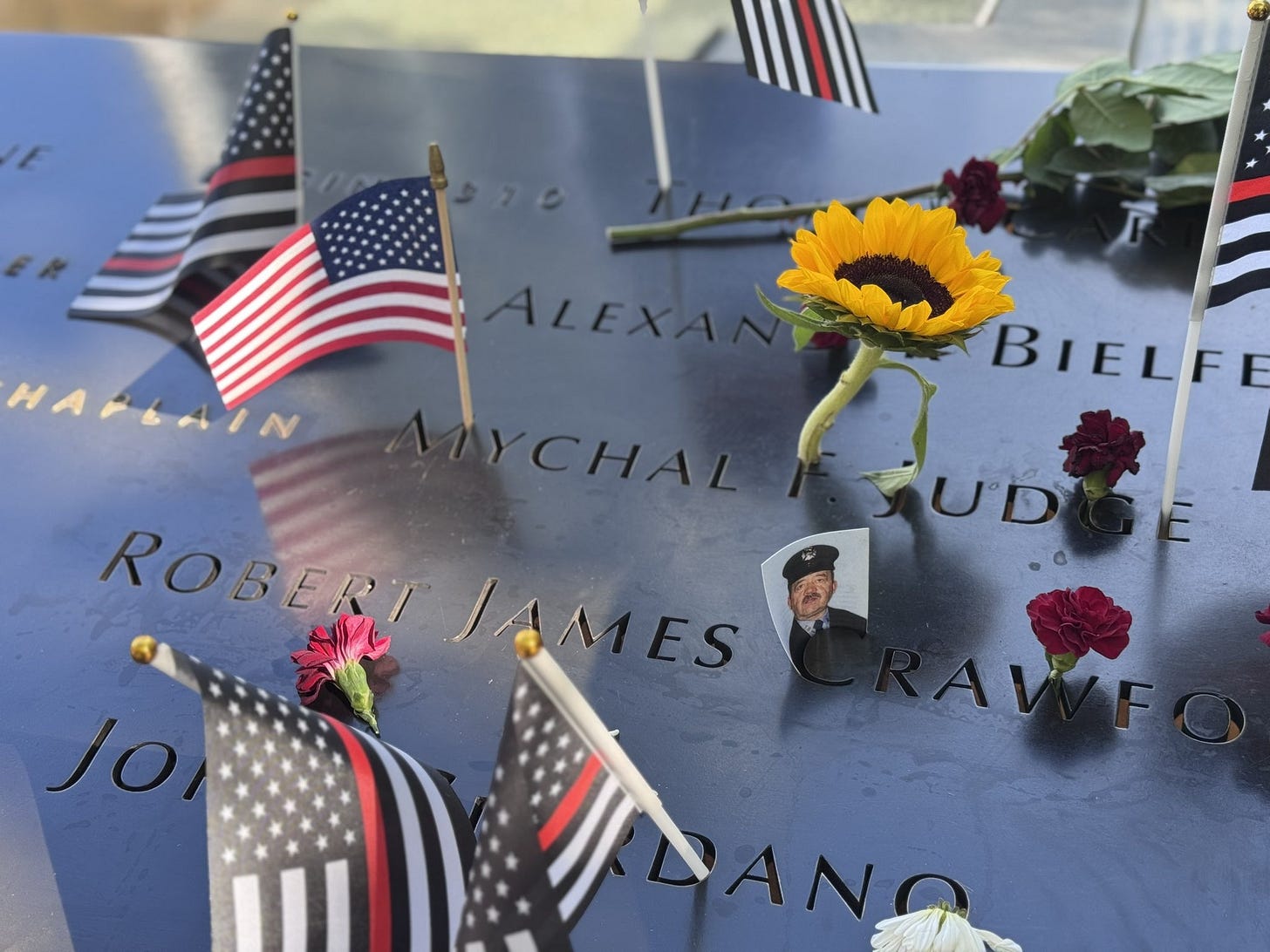 Father Mychal Judge’s name on the bronze parapet at the 9/11 Memorial, surrounded by flags and flowers