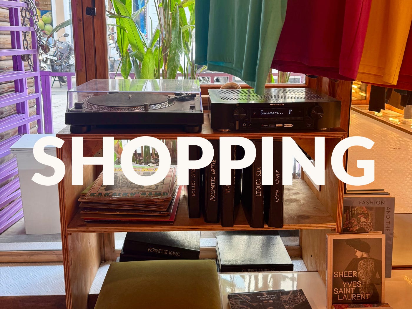Shop display shelf with books, a turntable, and colorful clothing, with “SHOPPING” text overlaid.