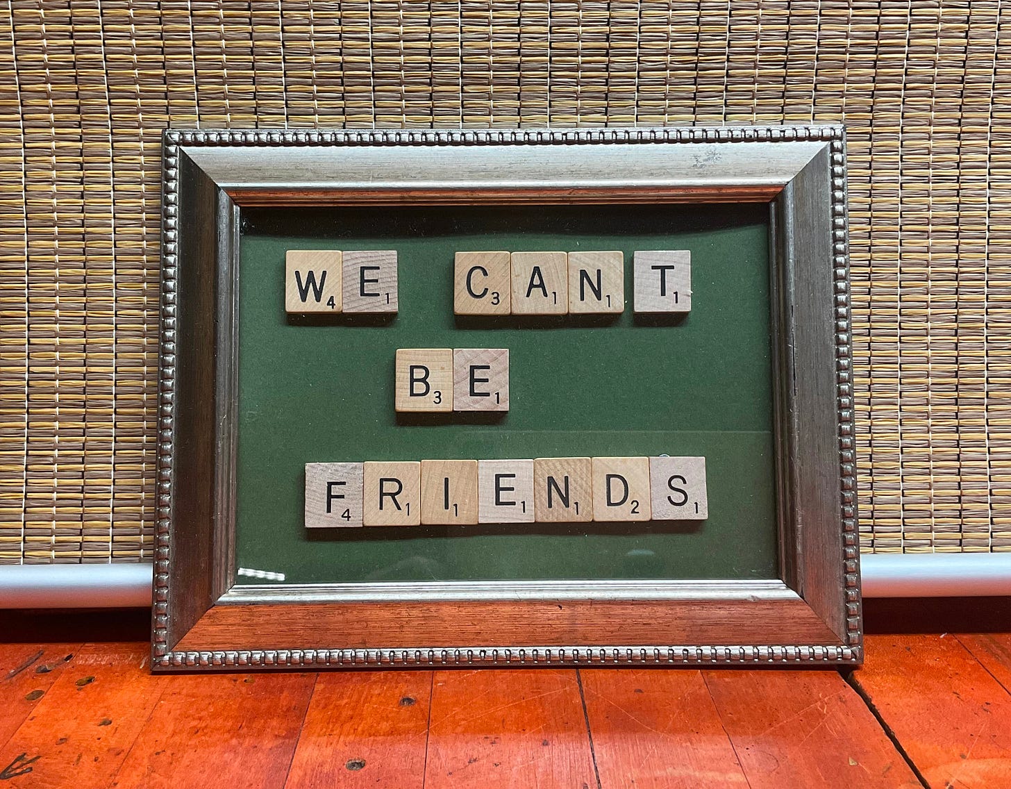 silver frame with green background with scrabble tiles spelling out "we can't be friends"