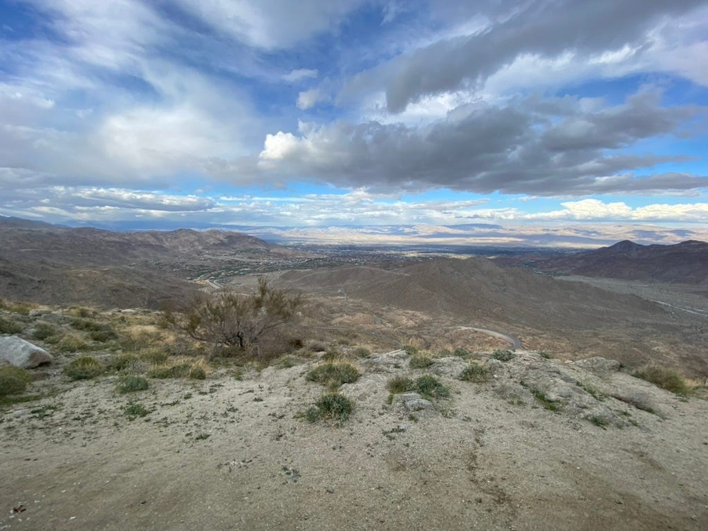 View from a mountain trail overlooking a Palm Springs, with layered hills and a cloudy sky stretching to the horizon. View from a mountain trail overlooking a Palm Springs, with layered hills and a cloudy sky stretching to the horizon.