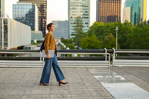 Businesswoman walking in urban environment Confident businesswoman walking in a modern cityscape, holding a laptop. She is surrounded by tall buildings and greenery, embodying a professional urban lifestyle stroll stock pictures, royalty-free photos & images