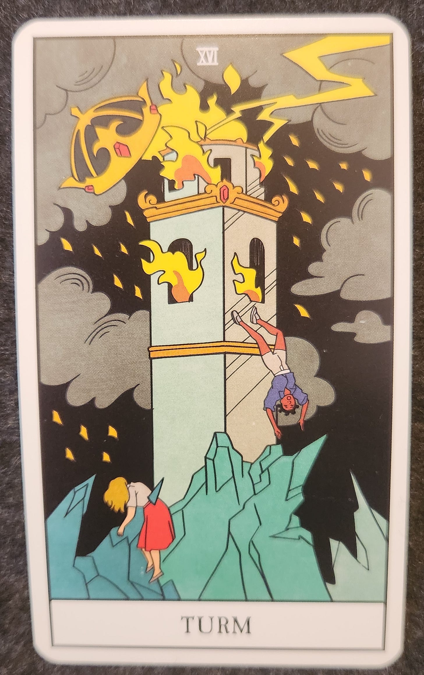 A tarot card labelled 16. The Tower. A tree has been struck by lightning. The top of the tree has turned to ash. The bottom of the tree is covered in green grass. Around the tree are multiple butterflies that appear to be forming from the energy of the lightning strike. There is a squirrel at the bottom of the tree looking up.