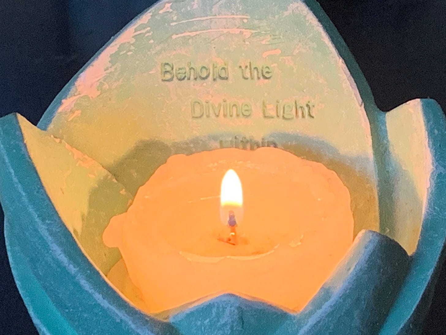 lit candle inside lotus-shaped ceramic candle holder inscribed with "Behold the Divine Light within" 