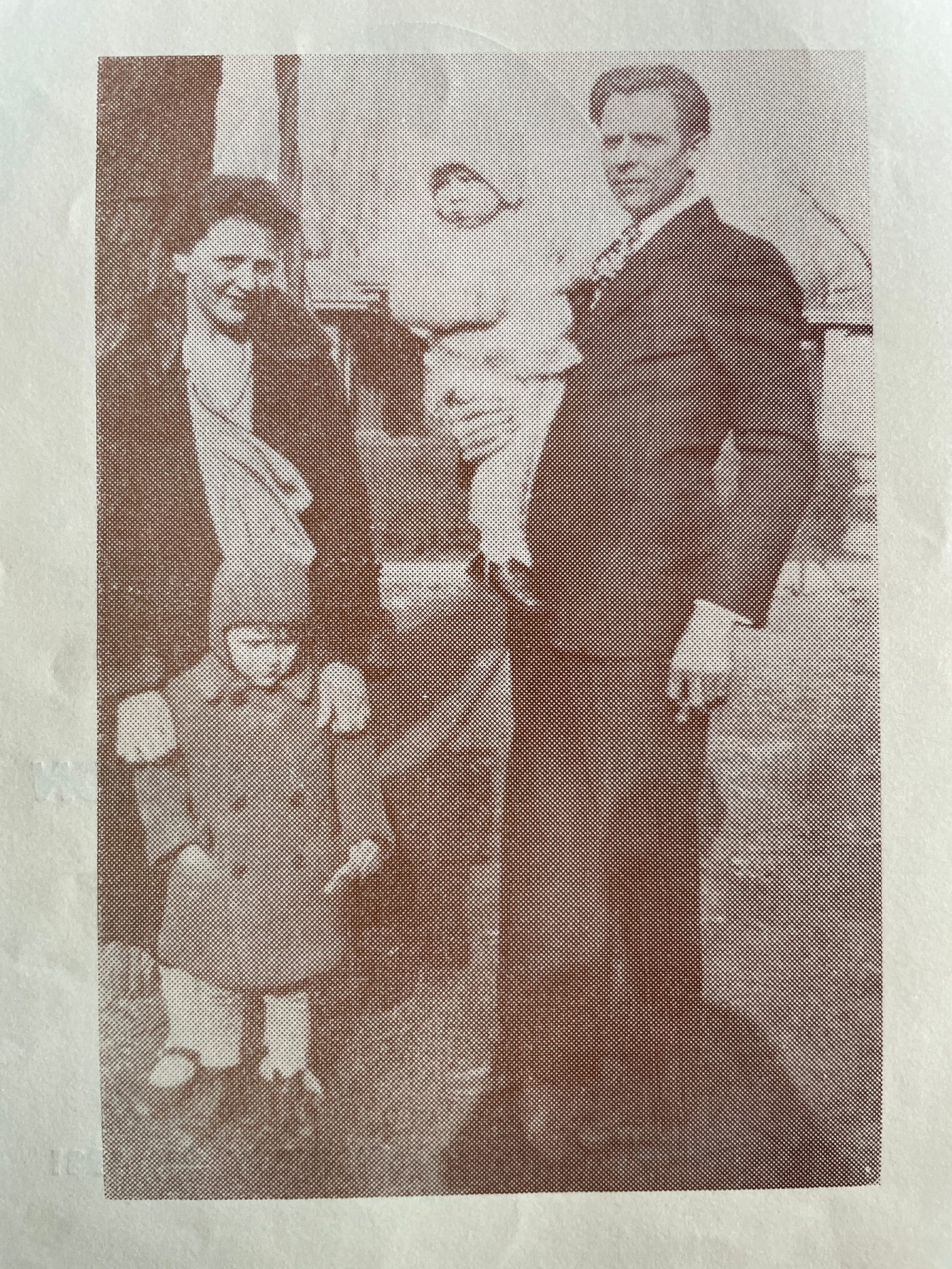 A sepia family portrait with a man in a suit holding a toddler standing beside a woman in a heavy coat, her hands on the shoulders of her young son who wears a cap and matching buttoned double-breasted coat.