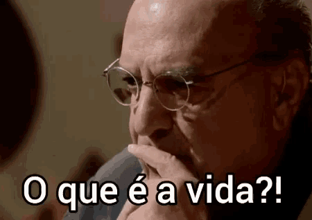 a man wearing glasses holds his hand to his chin and says o que e a vida ?