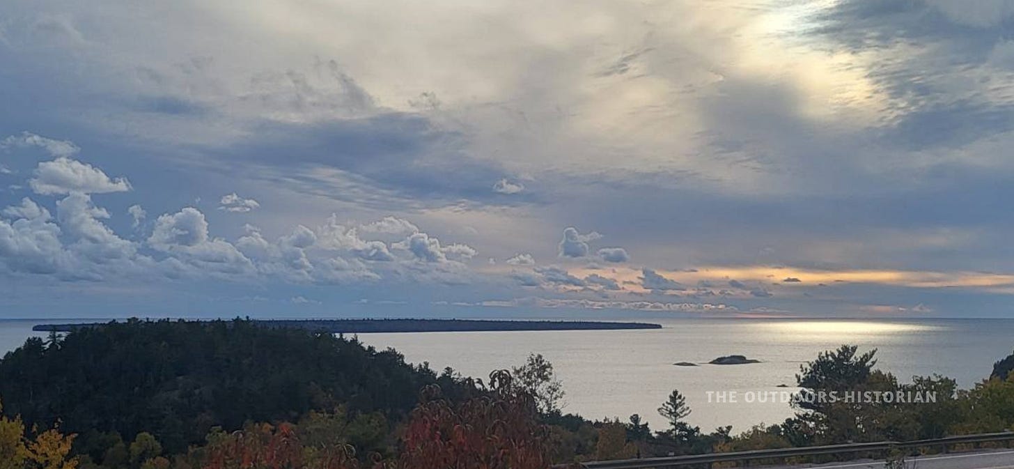 An elevated overlook view of Lake Superior under an unsettled sky with light breaking through the clouds and a view of the Agawa Islands on the horizon.
