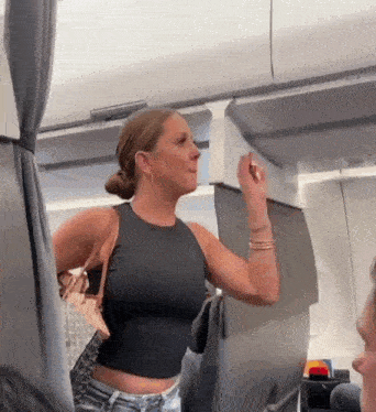 a woman in a black tank top is standing on an airplane talking to another woman .