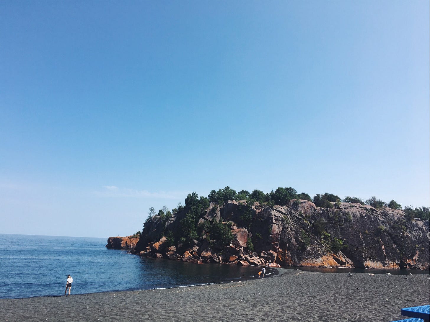 Picture shows the black sand beach with a mound of boulders in the distance. Picture shows the black sand beach with a mound of boulders in the distance.