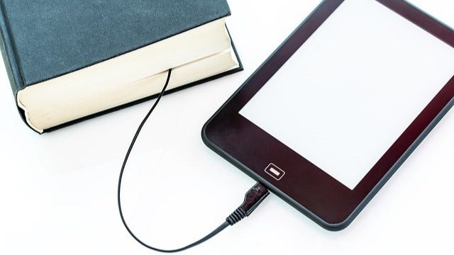 An ereader with a USB cable plugged into it. The other end of the cable is between the pages of a book. An ereader with a USB cable plugged into it. The other end of the cable is between the pages of a book.