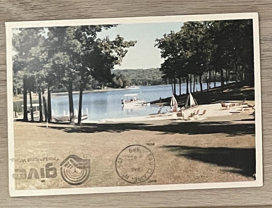 An old postcard of a lake surrounded by trees and boats on the water