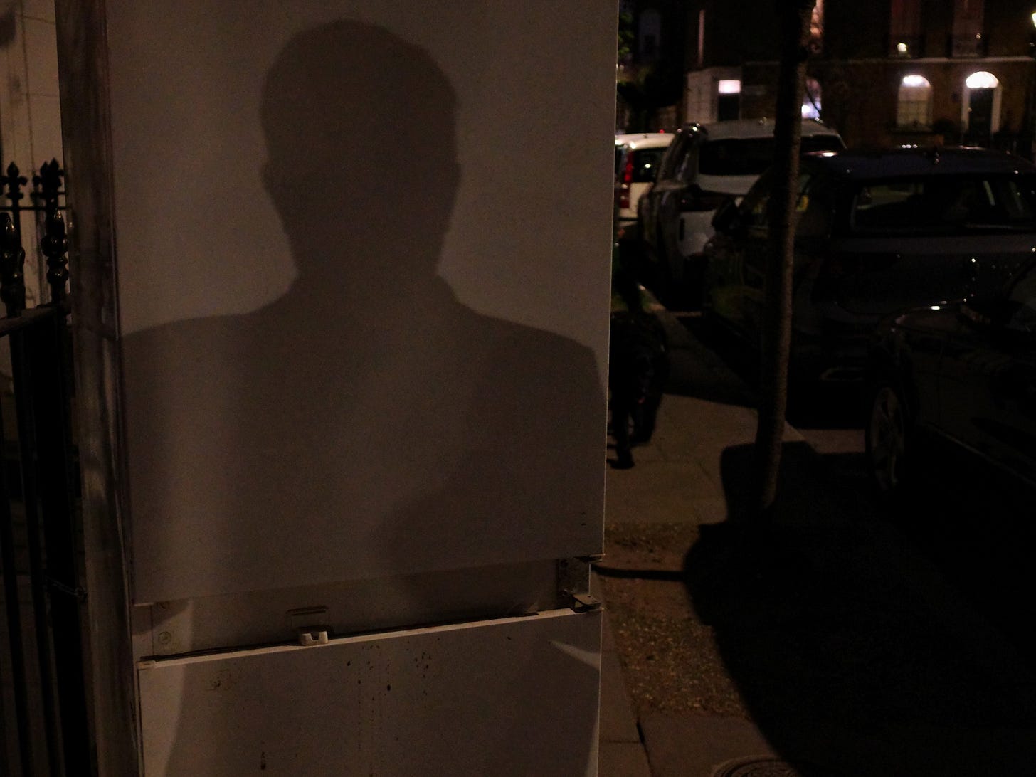 A man's shadow projected as a silhouette on the doors of a fridge. The fridge stands on a dark street A man's shadow projected as a silhouette on the doors of a fridge. The fridge stands on a dark street