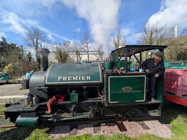 A small green steam train and some wagons, with blue sky