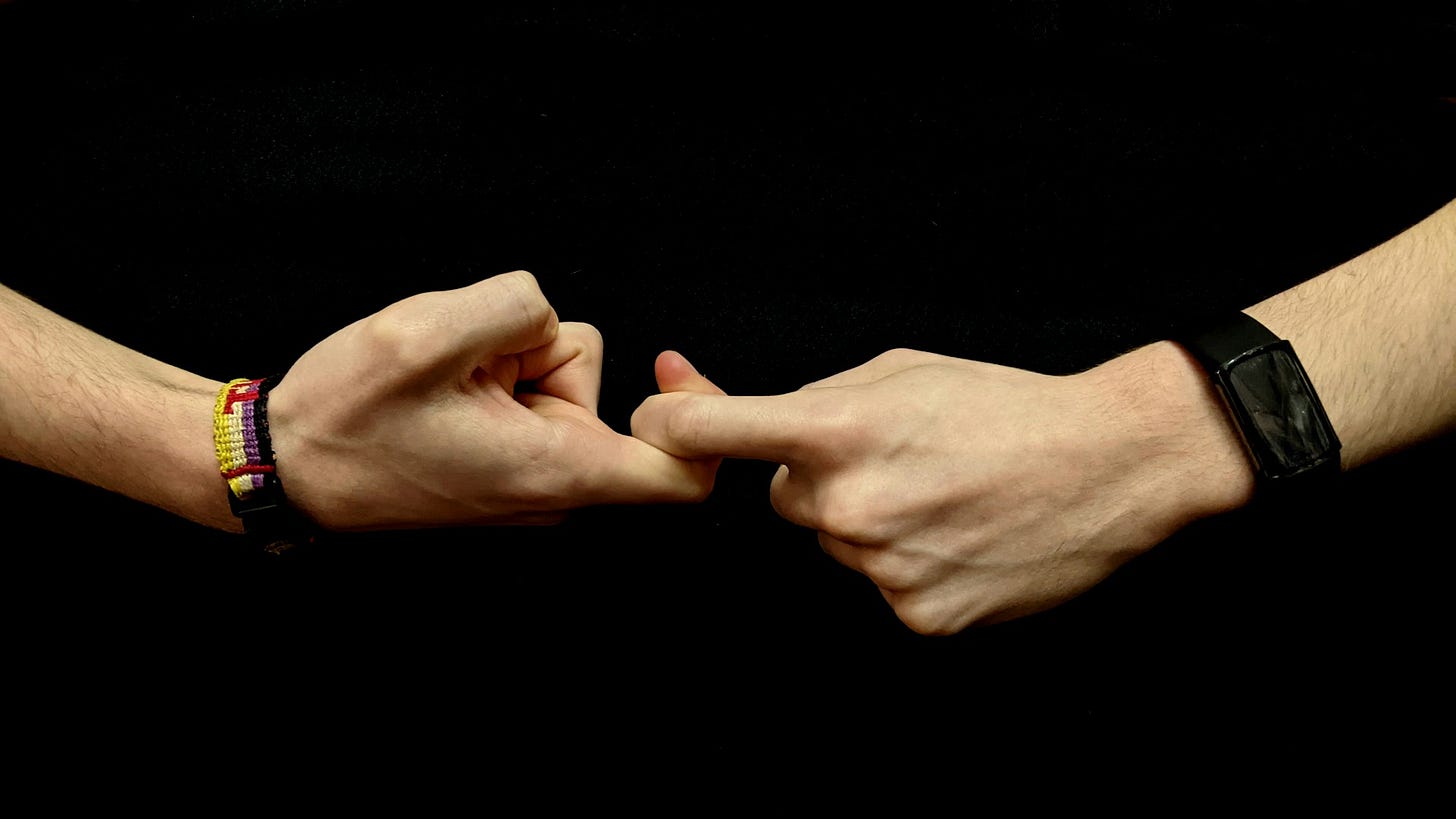 The hands of a young white person against a black background form the first half of the sign for “friendship” in American Sign Language.