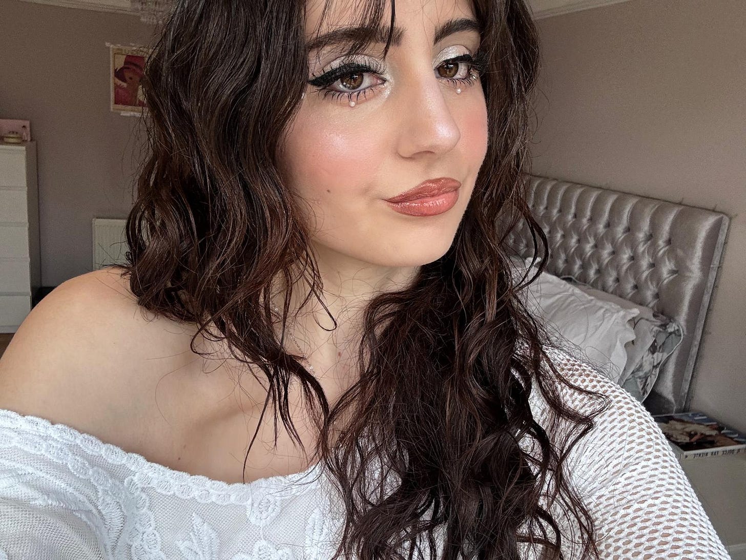 A portrait of Gia wearing a finished makeup look with shimmering silver lids, dramatic winged eyeliner, and small pearls placed under the lower lash line.