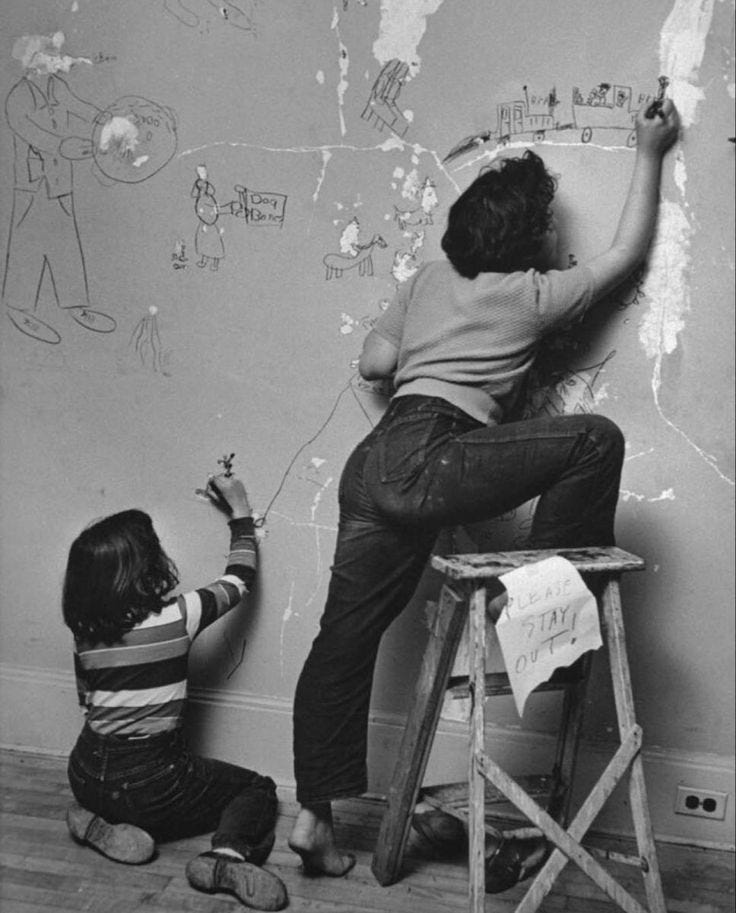 This may contain: two children are drawing on the wall with chalk and paint while one child is sitting on a stool