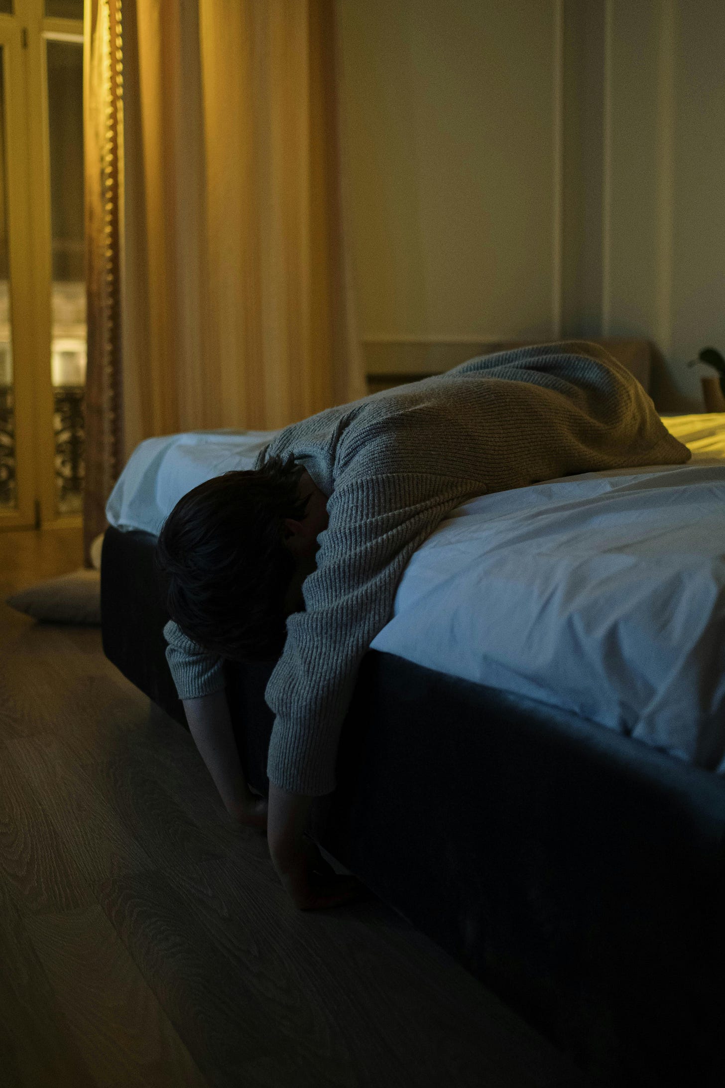 Person laying on their bed, face down, head draped over the edge of the bed. the room is dim, as it would be at night Photo by cottonbro studio: https://www.pexels.com/photo/person-in-gray-long-sleeves-lying-on-a-bed-6951529/