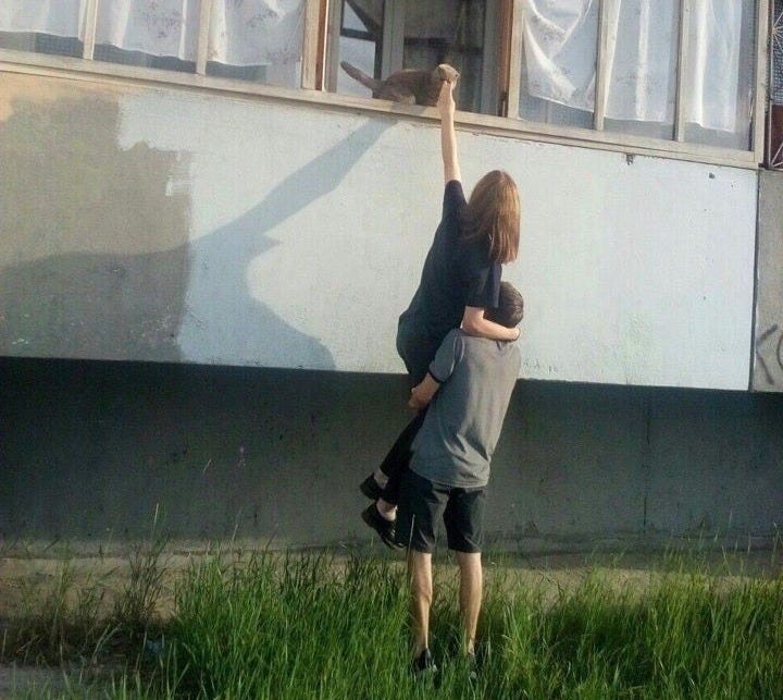 This may contain: two people reaching up into the air to reach something out of an open window in front of them