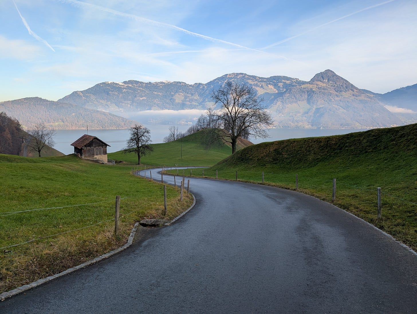 Winding road through green fields with lake and mountains in background Winding road through green fields with lake and mountains in background