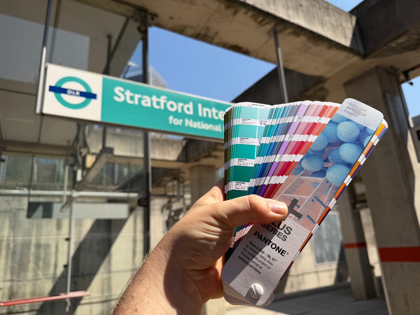Photo of a Pantone swatch book being held up against DLR signage.