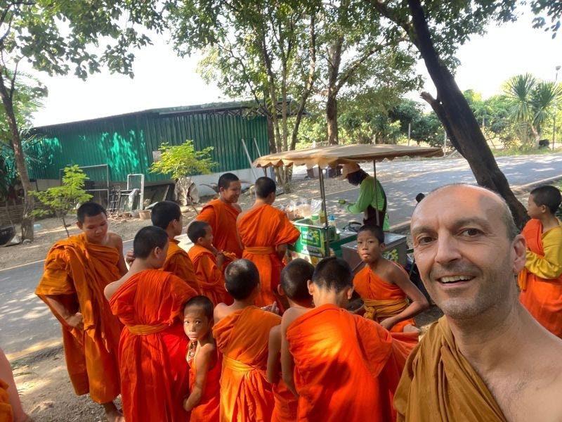 Monk standing in ice cream line smiling together with bunch of novice monks at a Buddhist temple in nothern Thailand