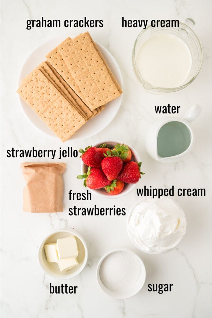 Top view of ingredients on a white surface, including graham crackers, heavy cream, water, strawberry jello powder, fresh strawberries, whipped cream, butter, and sugar. Each item is labeled with black text.