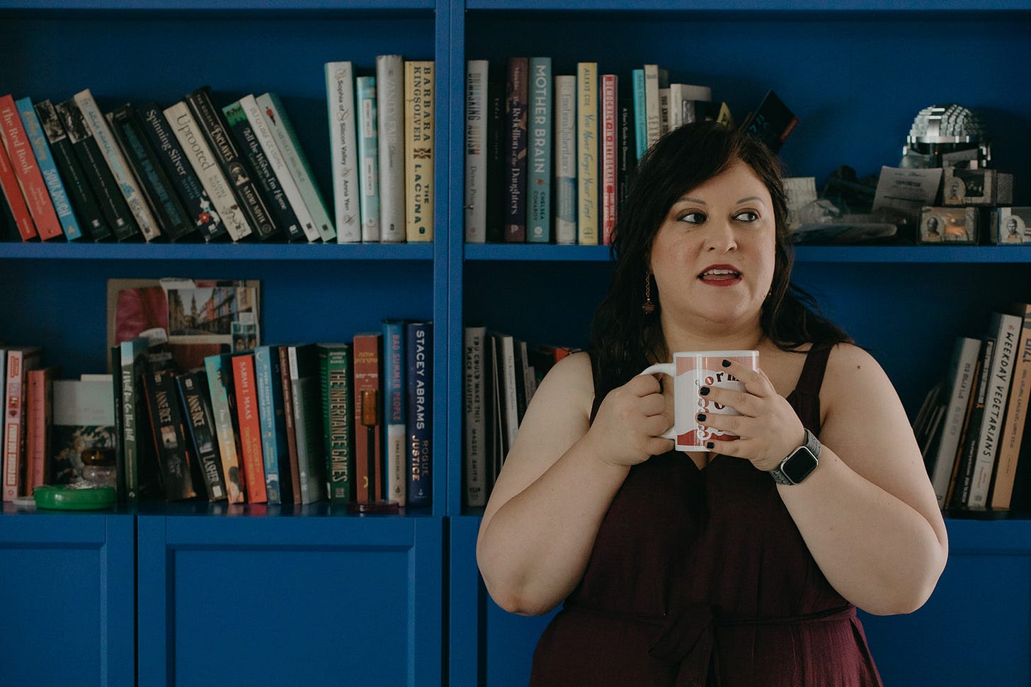 chedva (vivi) holding a coffee mug in front of a cobalt blue library