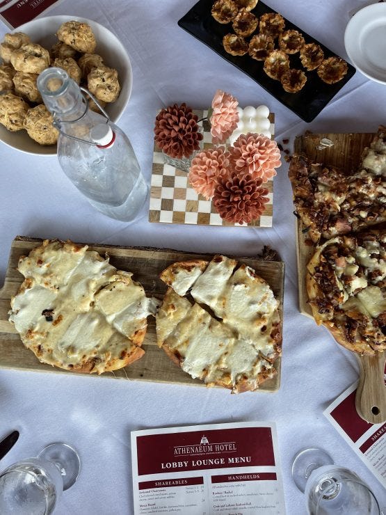 An elegant spread from the Athenaeum Hotel's Lobby Lounge menu featuring flatbreads, appetizers, and decorative touches on a crisp white tablecloth, highlighting the hotel's refined dining experience. Photo credit: Tamara MC, Ph.D.