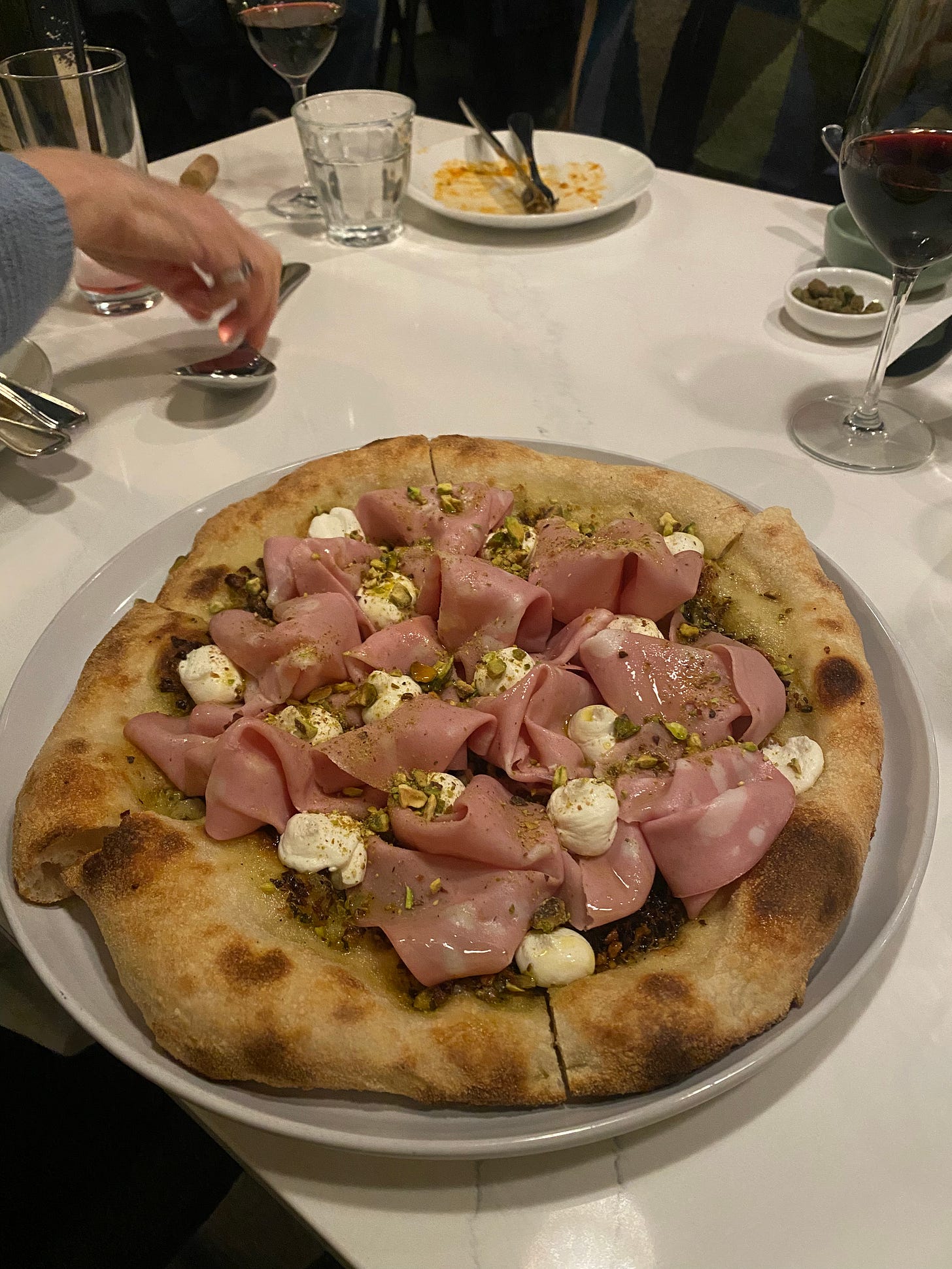 A mortadella and pistachio pizza on a large plate.