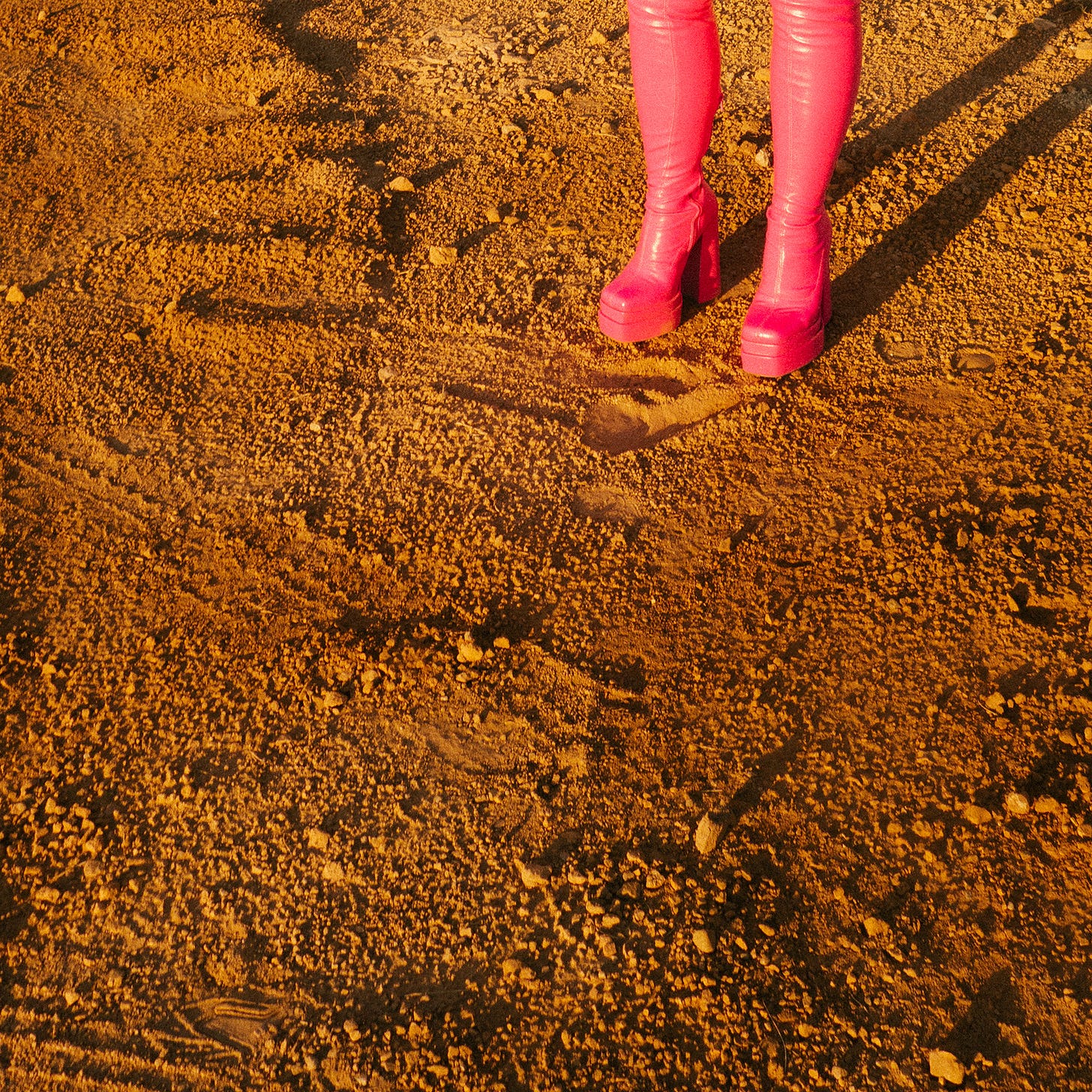 A close-up of a pair of bright pink pleather boots standing on cracked, dry earth. A close-up of a pair of bright pink pleather boots standing on cracked, dry earth.
