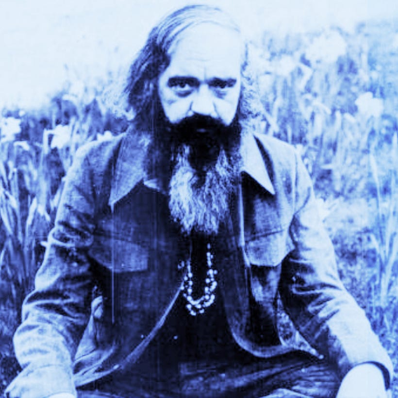 Photo of British cybernetician Stafford Beer sitting cross-legged in the grass in 1975.