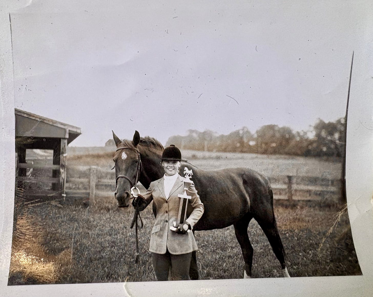 Horse and rider standing in a field, rider holding a tropphy