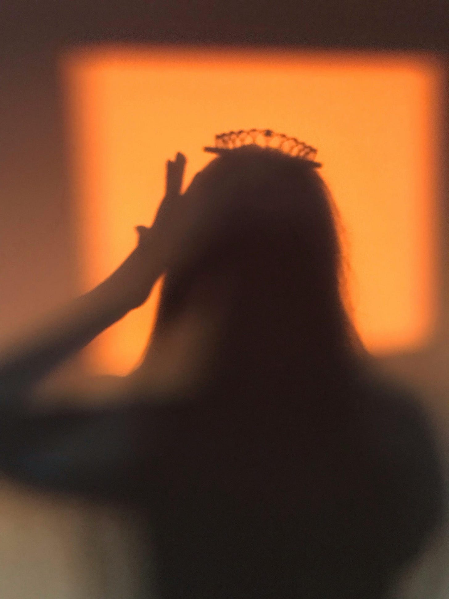Free A silhouette of a person wearing a crown with a warm orange background. Stock Photo