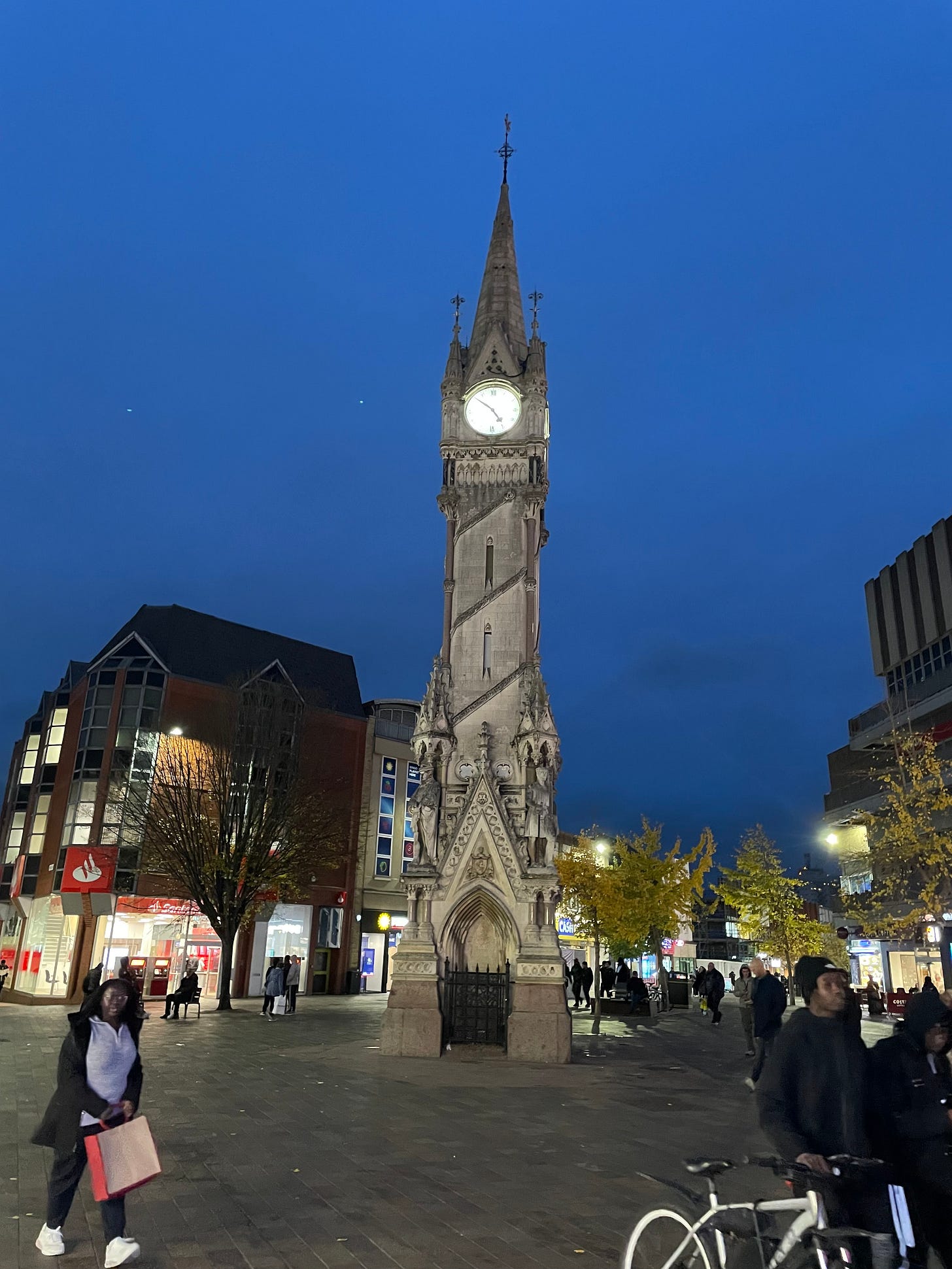 The clocktower in Leicester City Centre in the dusk (the clock reads about 4.55 pm) with lots of people going about their business.