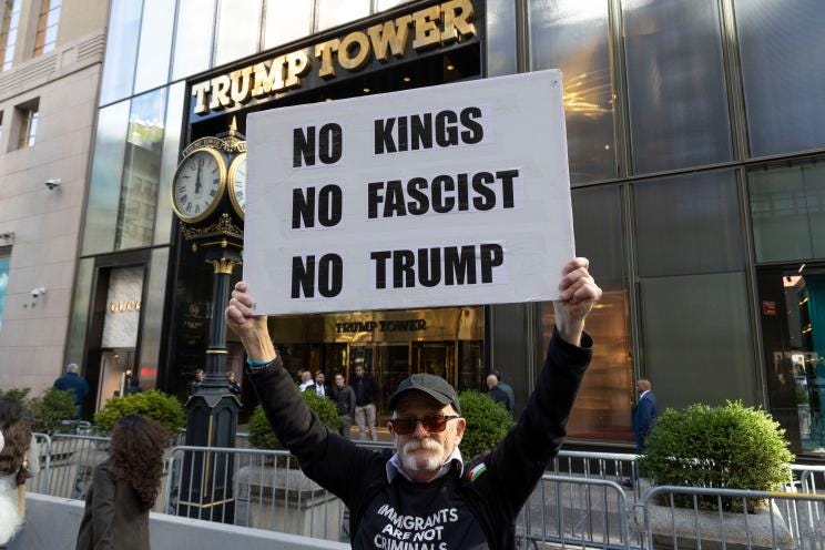 An anti-Trump demonstrator holding a sign that reads "NO KINGS NO FASCIST NO TRUMP" outside of Trump Tower.