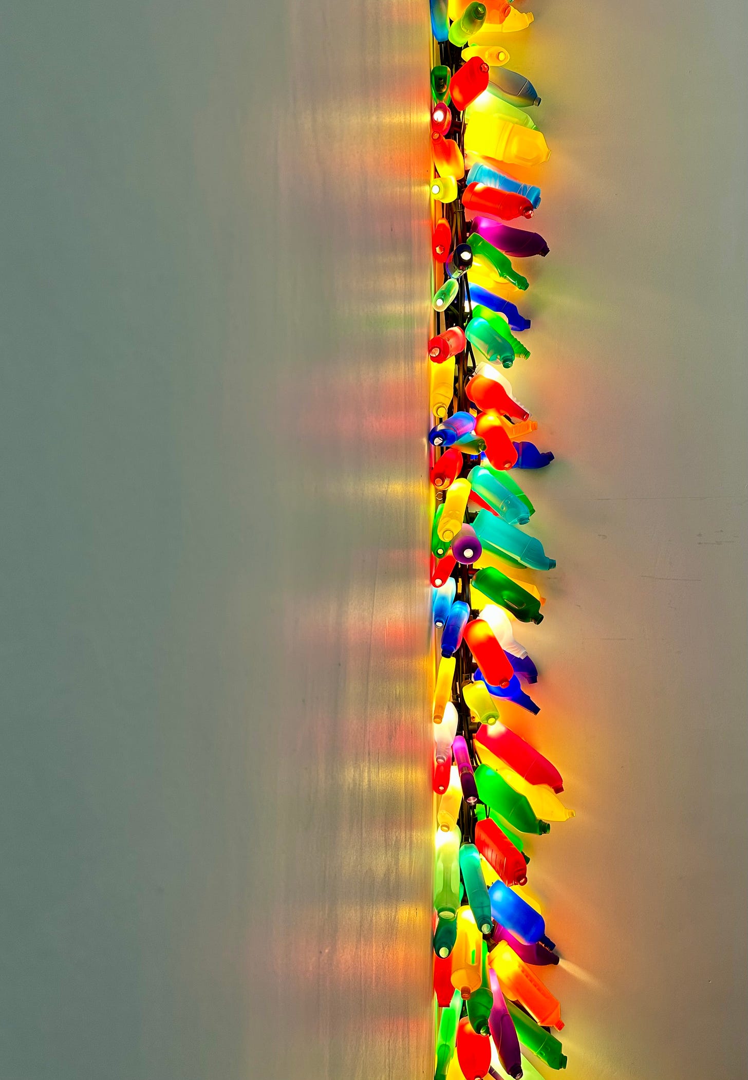 Plastic bottles or various colours fastened together to form a continuous thread, are illuminated, so they appear to be like a Christmas decoration.