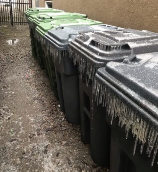 A row of large garbage bins covered in icicles.