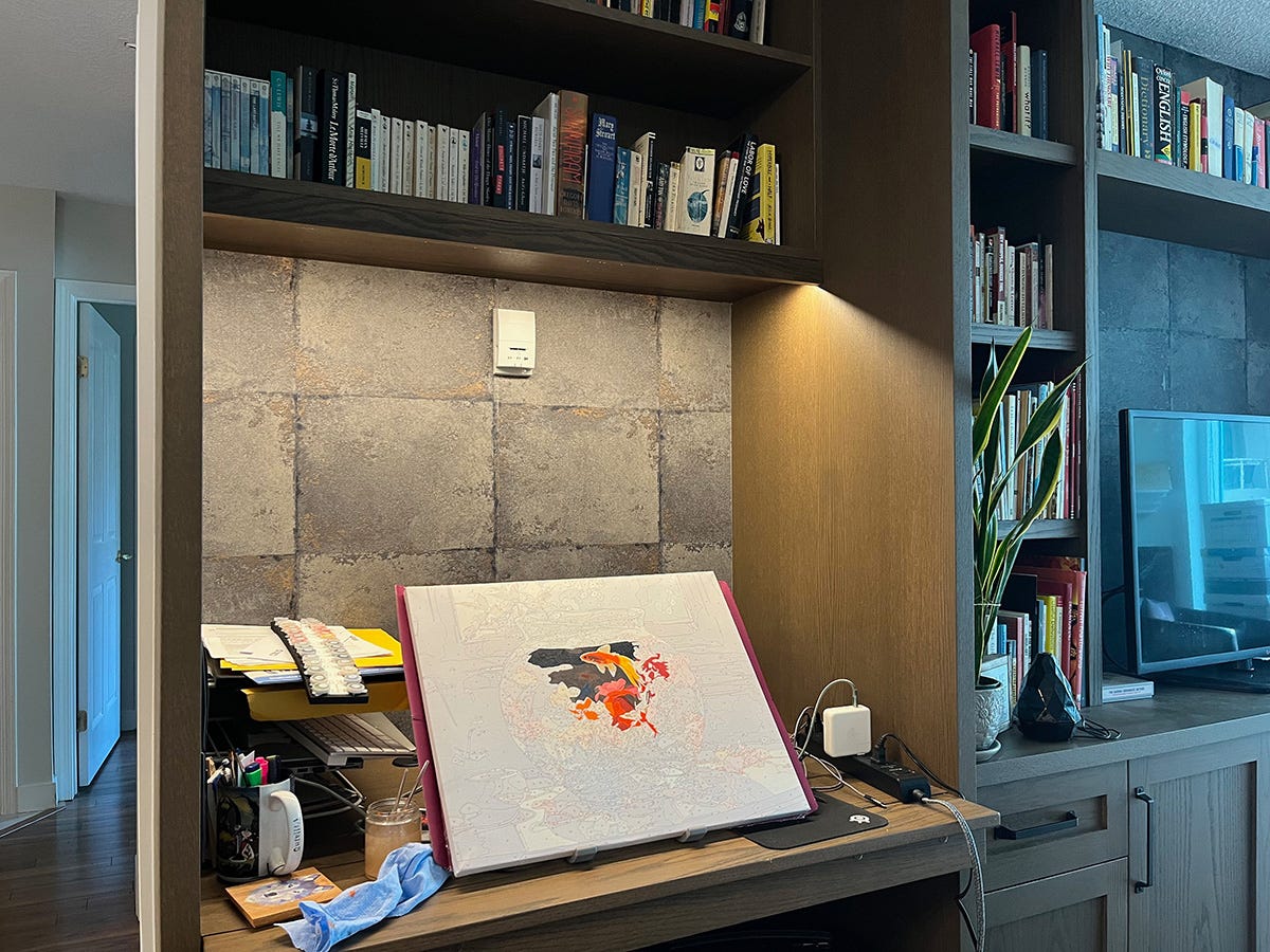 The paint by number with the goldfish sitting in a small work area that's part of a large wall unit. The wall unit also has lots of bookshelves, cabinets and a flat screen TV.
