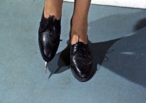 black shoes at the end of a woman's legs. the one on the left has a poisoned steel blade sticking out of it.