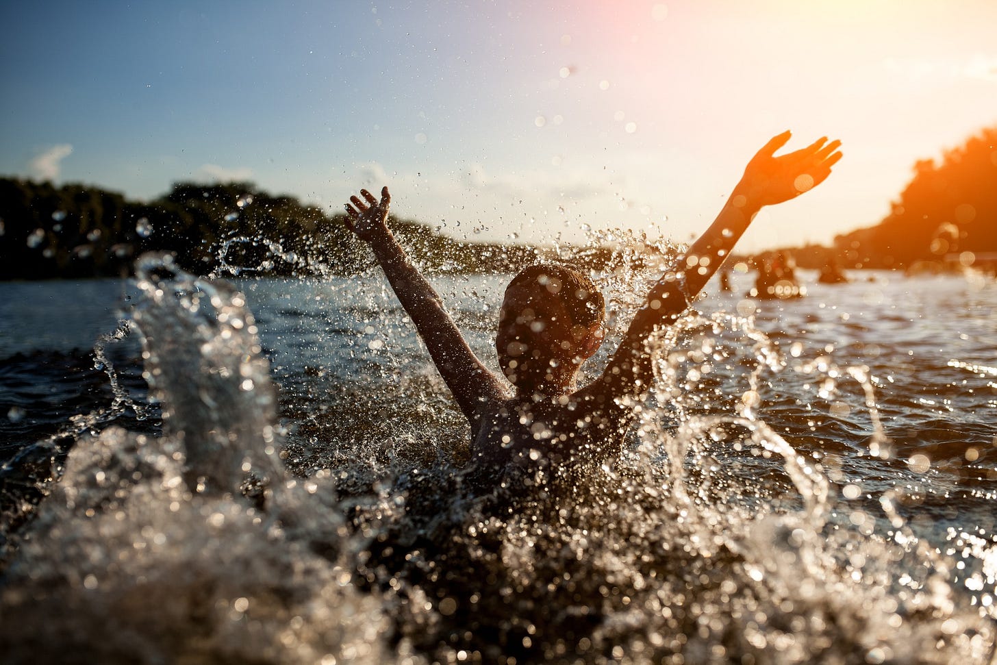 Child splashing in a lake, silhouetted against a setting sun