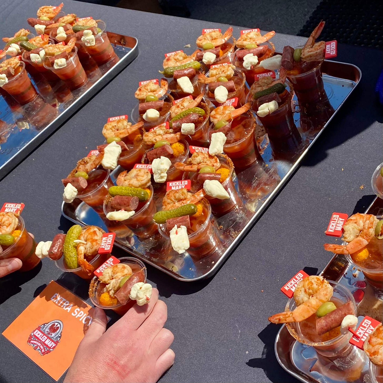 A tray of Extra Spicy Kickled Marys, with hands reaching forward to take sample cups.